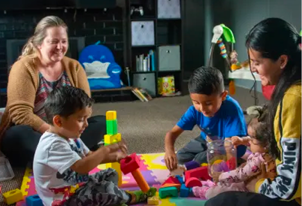 Image of A teacher and parent playing in block center with 3 children of various ages